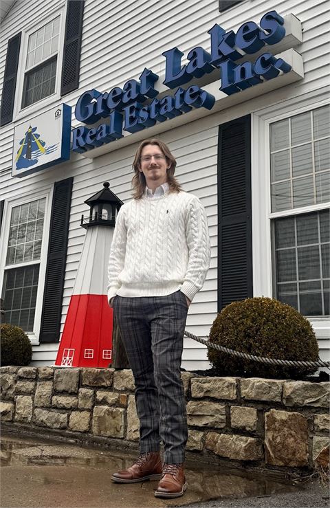 Garrett Lester standing outside the Great Lakes Real Estate office in Lewiston, New York, beneath the brokerage's lighthouse sign.